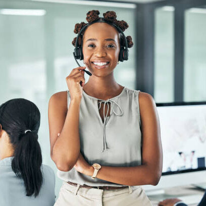 Friendly call center agent standing with arms crossed, looking proud and wearing a headset in an office with colleagues. Portrait of a smiling female customer service working looking confident